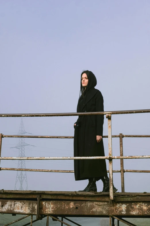 a woman in black standing on the edge of an old metal railing