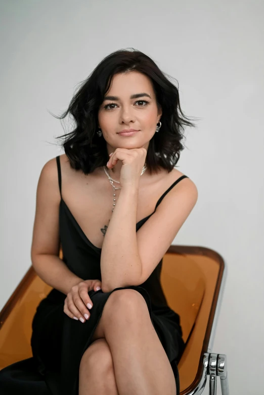 a women wearing a black dress is posing on a chair