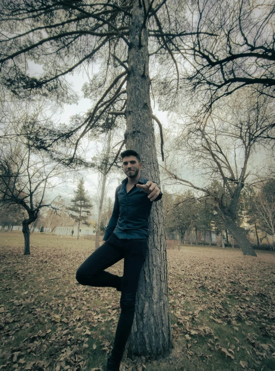 a man in black jacket leaning up against a tree