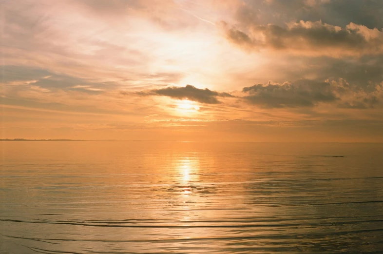 a small sailboat floating in the ocean as the sun sets