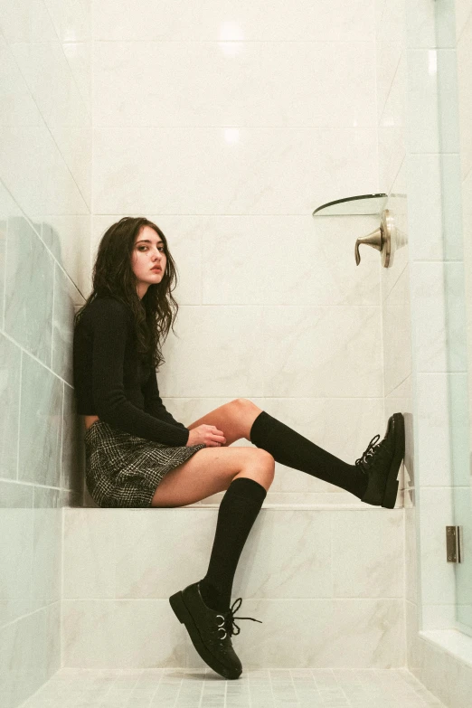 a young woman is sitting in a shower while she is wearing knee high boots