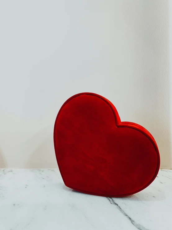 a red heart sculpture is on a white marble surface