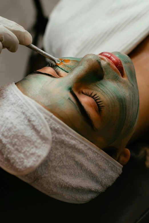 a woman getting a face mask with green pigment on her face