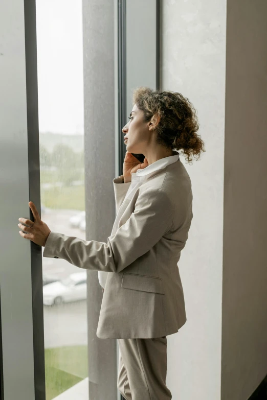 a woman in a suit is standing near a glass window