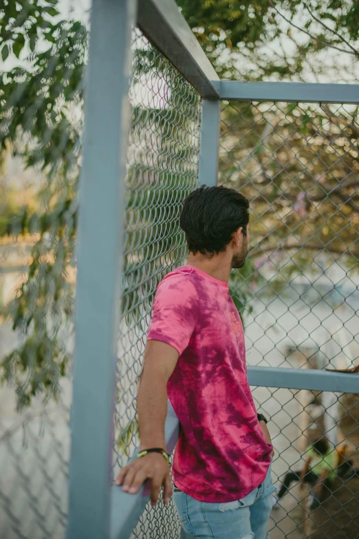 man in pink shirt leaning up against a fence