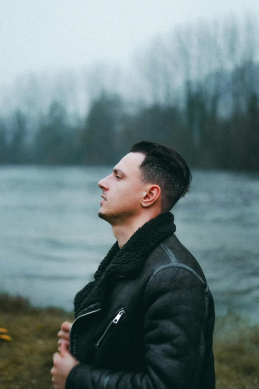 man in leather jacket sitting by a body of water