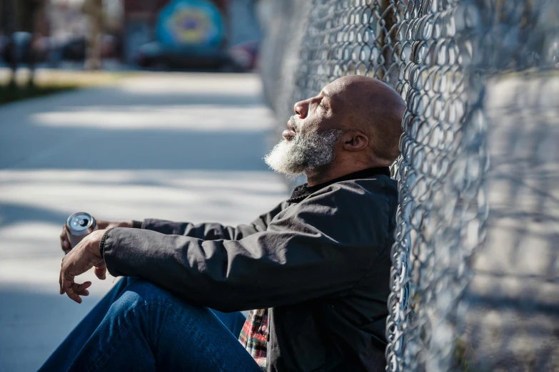 a man wearing a jacket and sunglasses leans on a fence