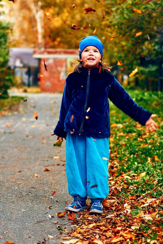 a child throws leaves as they walk on a paved path