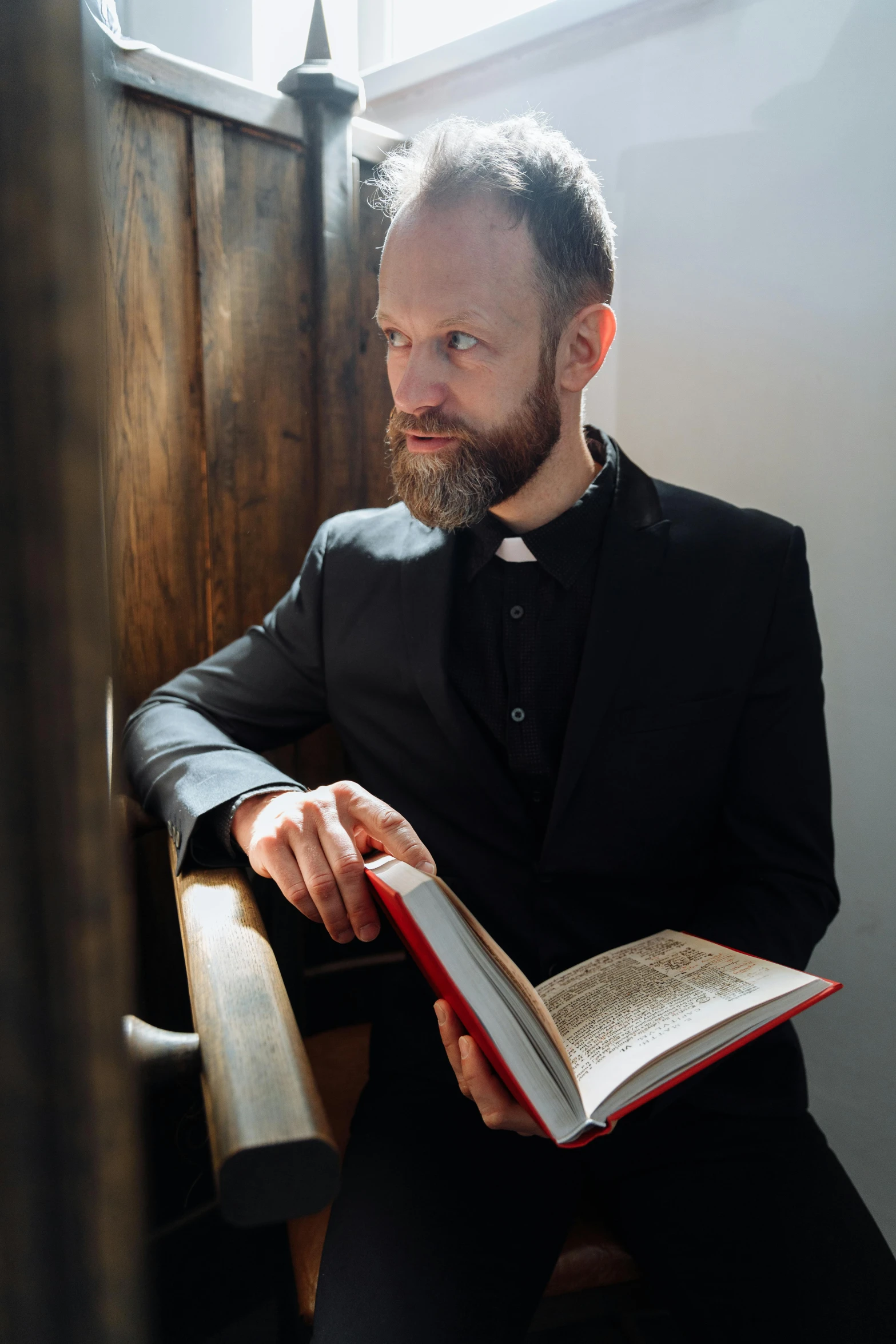 man with beard holding open book and sitting on a bench