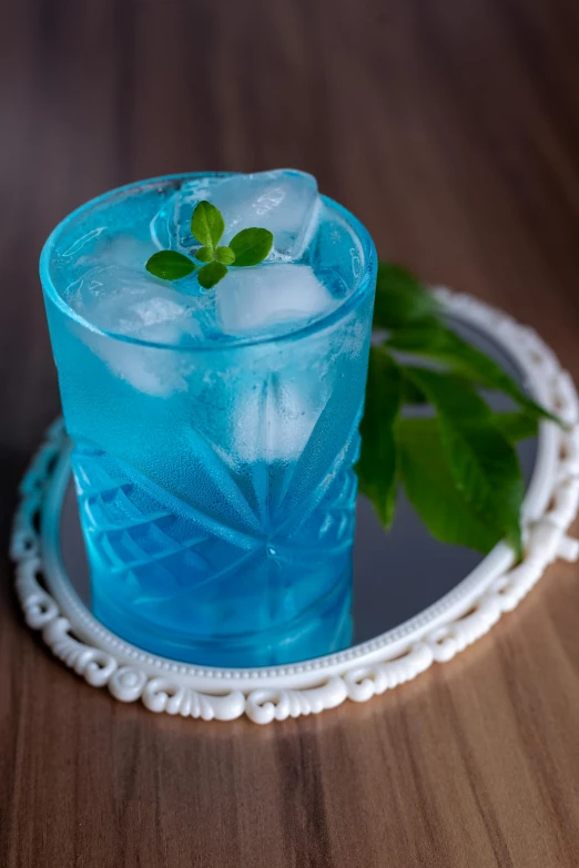 a drink is made with light blue alcoholic liquid, ice, and a sprig of mint