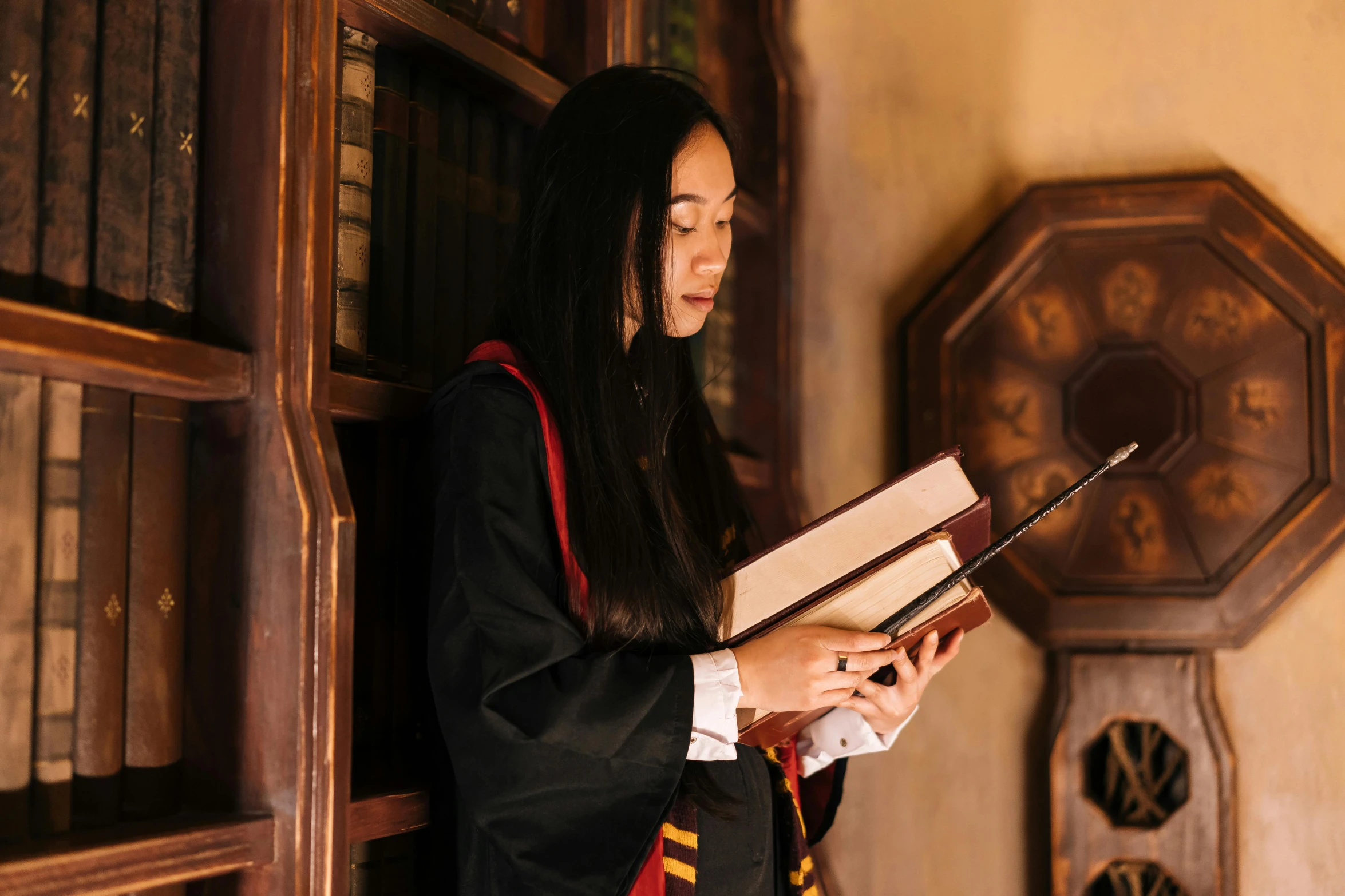 a female graduate holding three books in front of a bookcase
