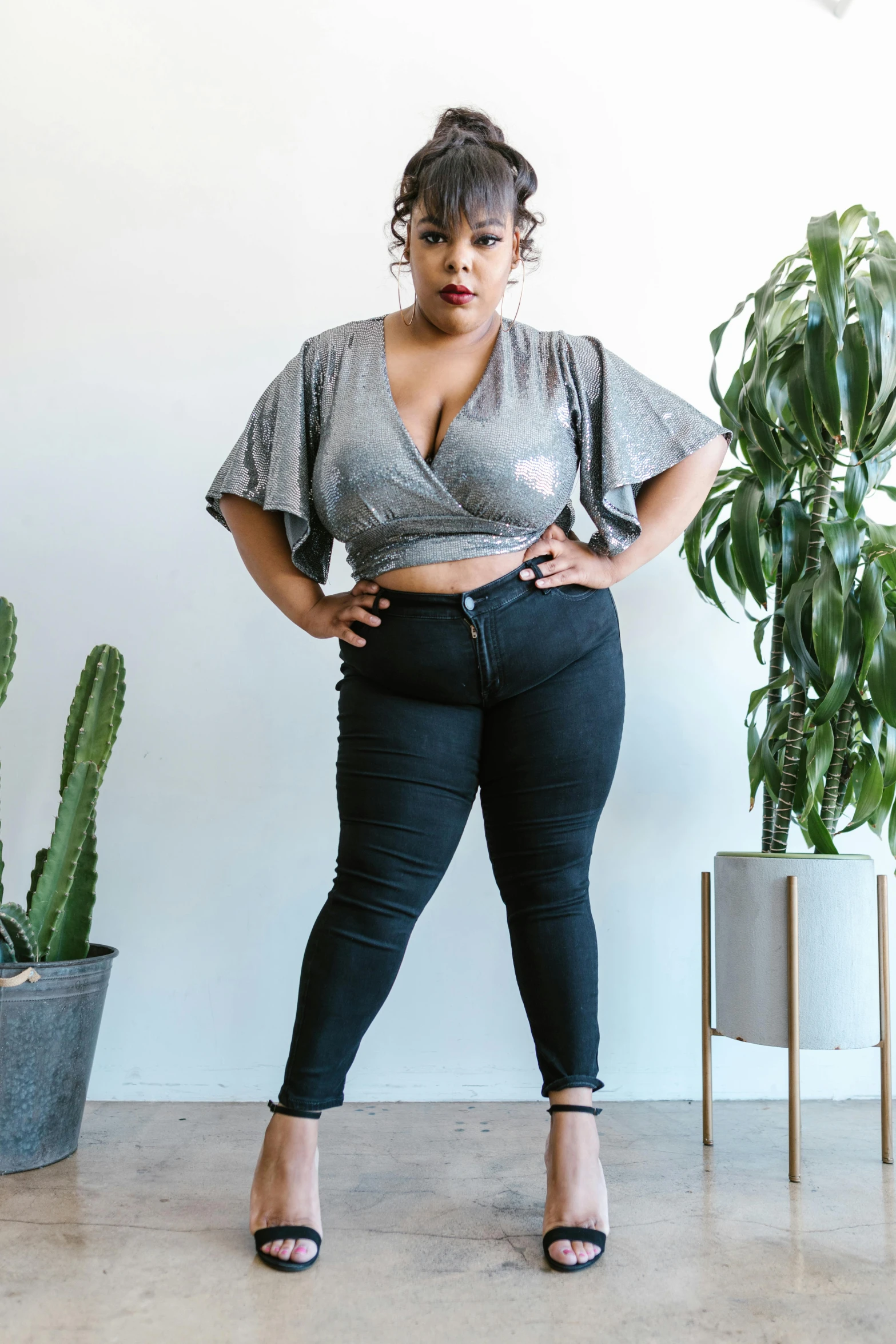 a woman in black pants standing next to a cactus