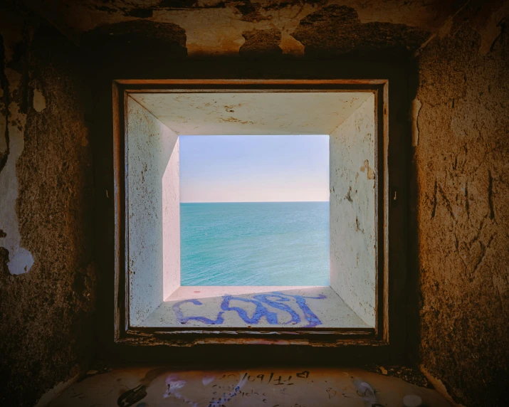 a window with graffiti sitting in a wall next to the ocean