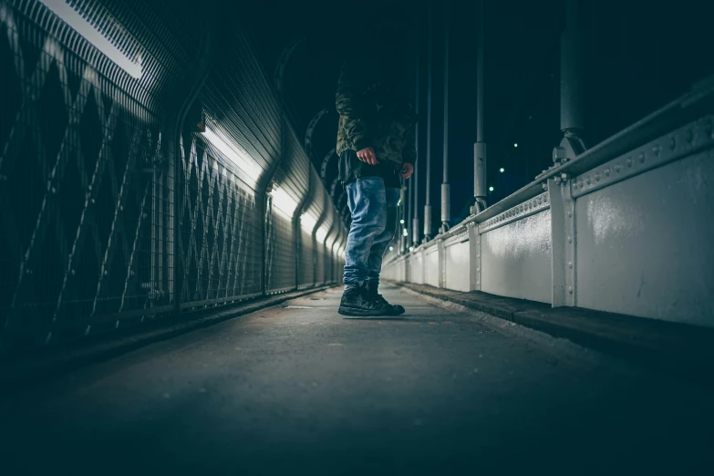 person walking on roadway at night with light coming through fence