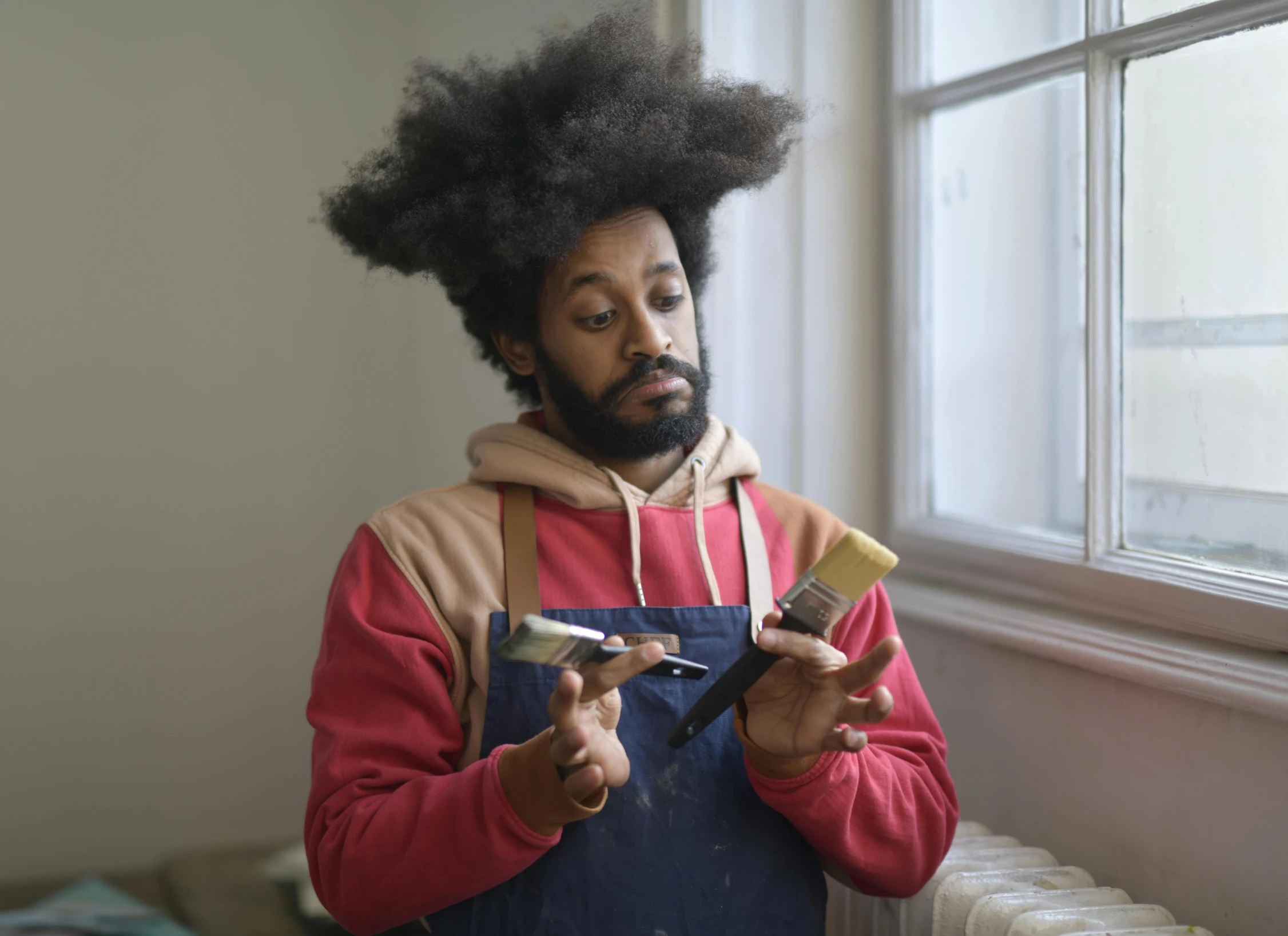 there is a man wearing hair while he is holding two different brushes