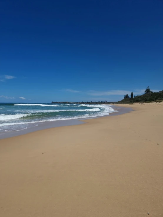 a sandy beach with waves coming ashore and houses in the distance