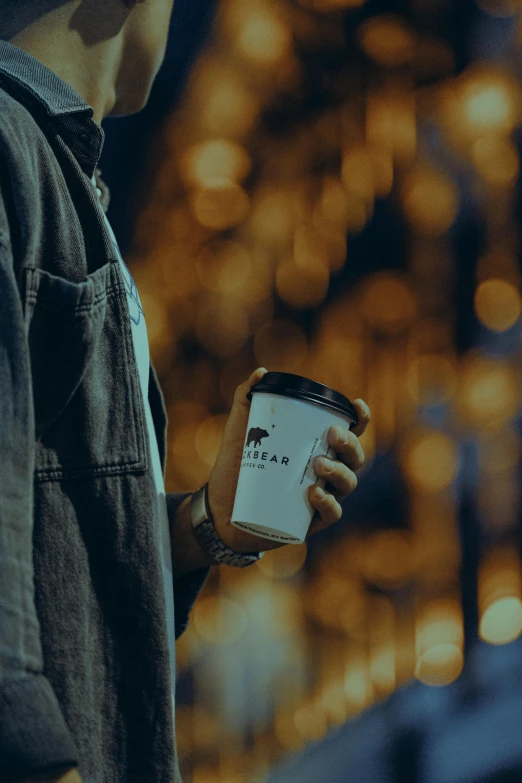 person holding an empty coffee cup standing in front of blurred lights