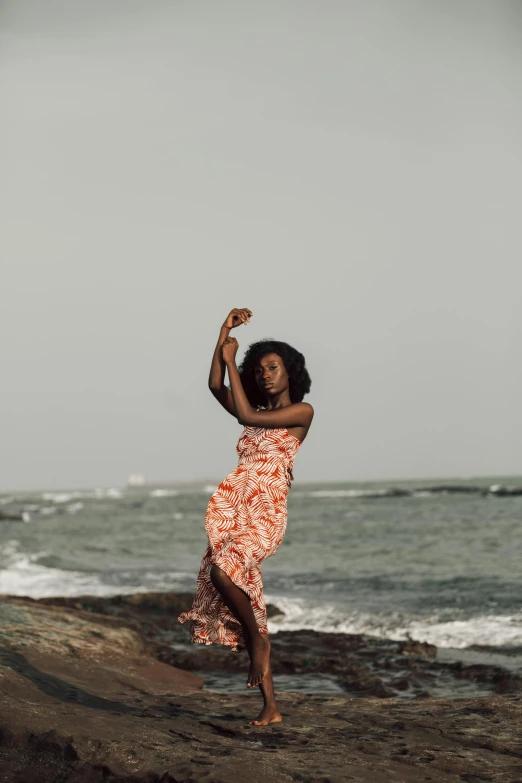 woman in orange and red dress dancing on rocks next to the ocean