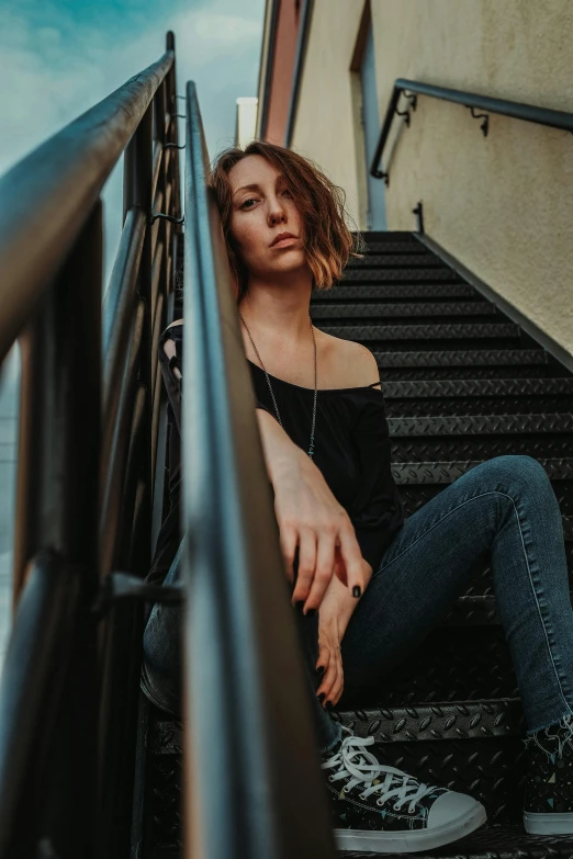 woman sitting on stairwell rail at dusk wearing converses