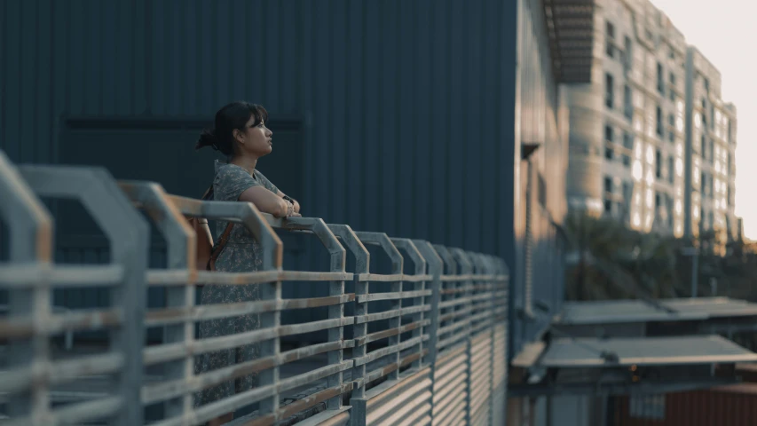 a girl standing at the edge of a metal railing next to buildings