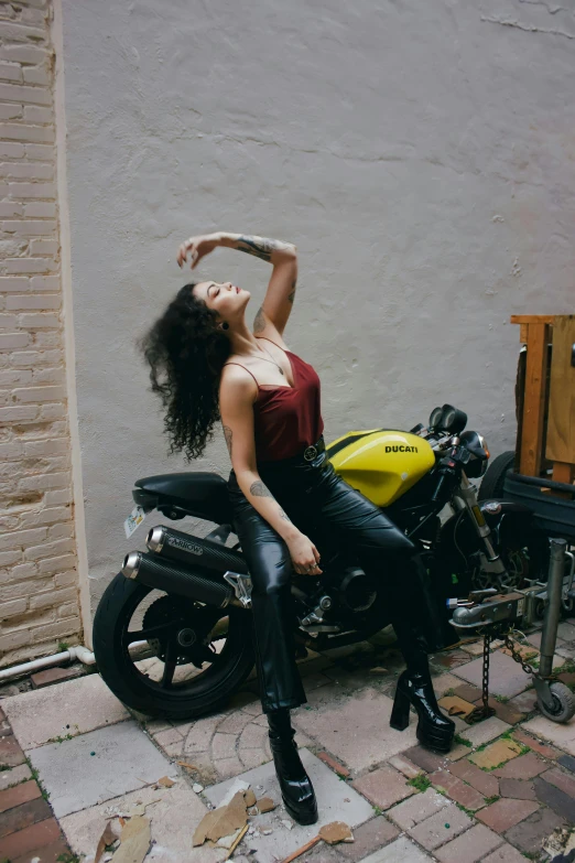 a beautiful woman in black pants and a red tank top sitting on a motorcycle