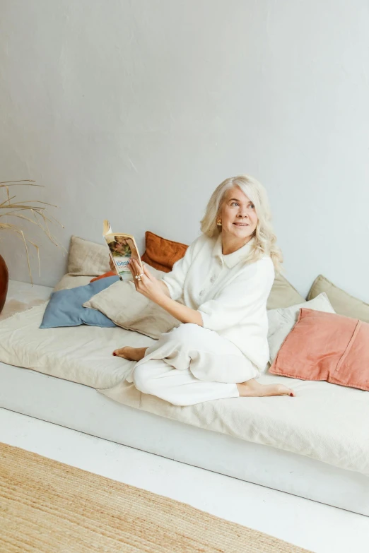 woman sitting on white bed smiling and reading