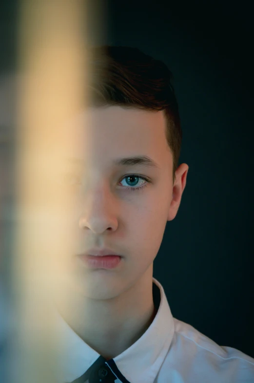 a young man standing against a dark background looking at the camera