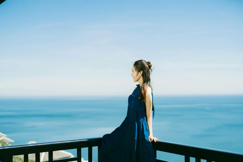 woman in long blue dress standing on deck overlooking water