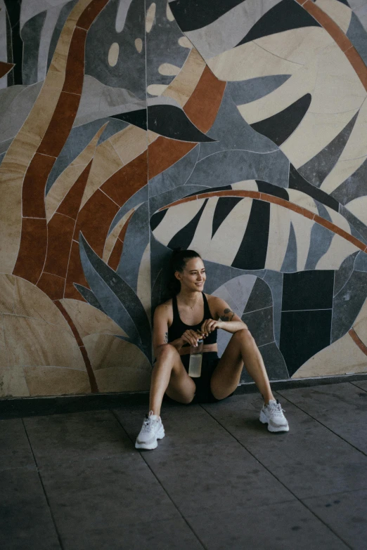 a woman wearing sports  with white sneakers, leaning against a mural