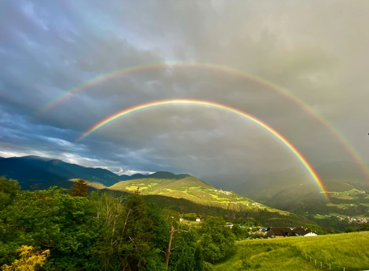 two rainbows, with a cloudy sky behind them