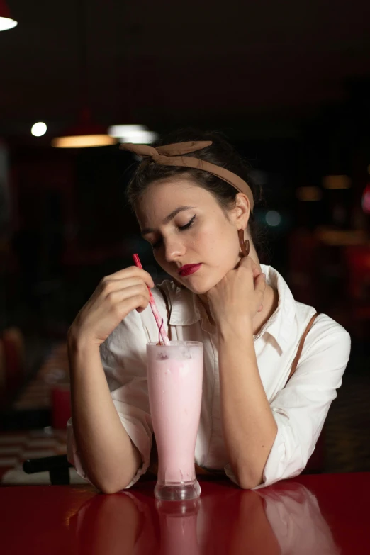 a young lady sitting at a table drinking a glass of milkshake