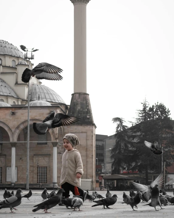 a young person is standing with pigeons and some are trying to feed