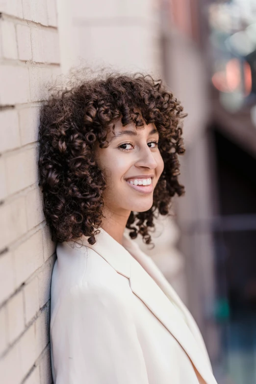 a woman in white is leaning against a brick wall