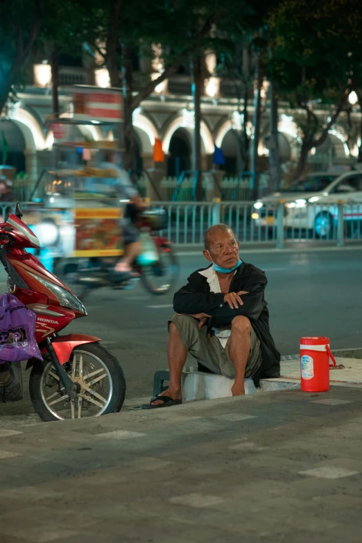 a man sitting on the edge of a road next to his scooter