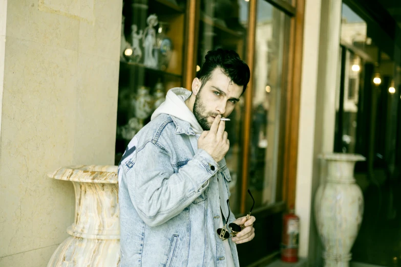 a man wearing a jacket smoking and standing in front of store