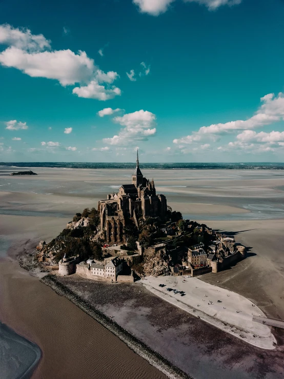 a bird's eye view of a beach area with rocks and a tower like building in the sand