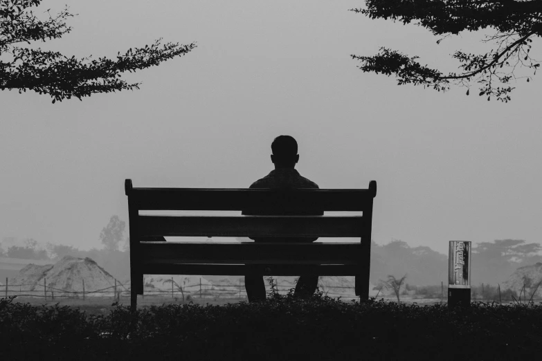 a black and white po of a man sitting on a park bench