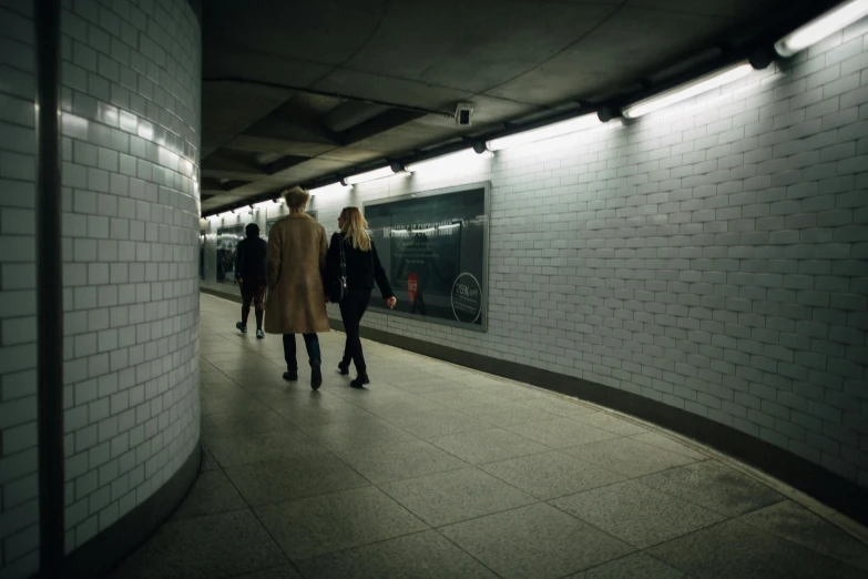 two women in long coats are walking along a subway