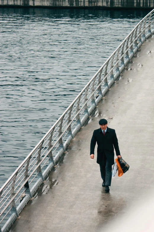 a man holding two bags walking down the side of a bridge