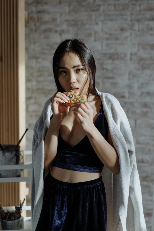 a woman standing in front of a white brick wall eating a pizza