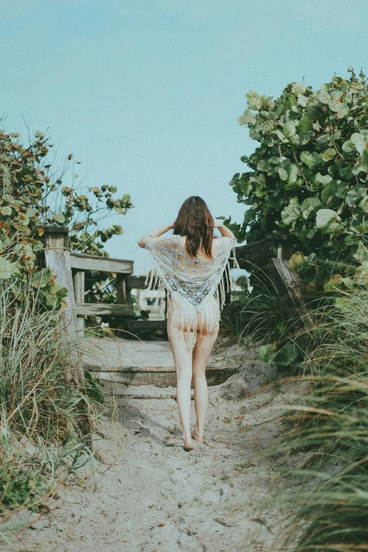 a woman walking down a dirt path near bushes