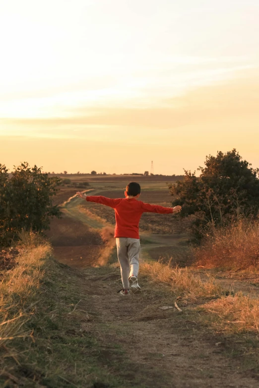 young man wearing red jacket running on road toward field