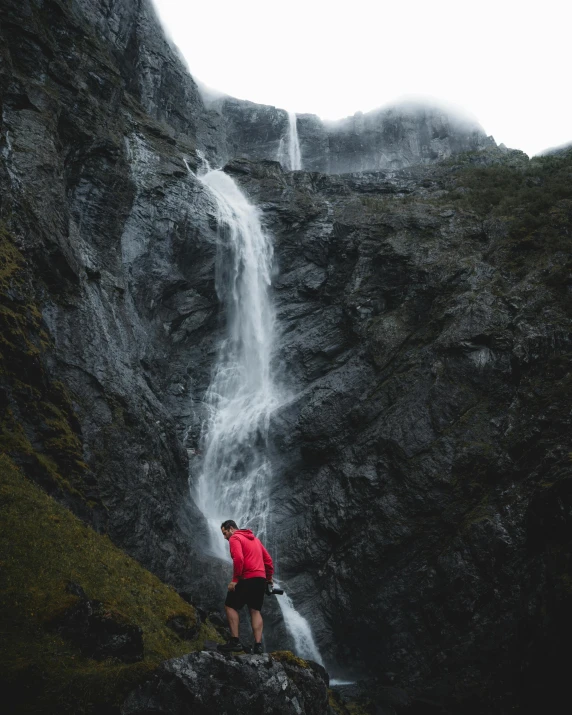 a man stands on a rock near a large waterfall