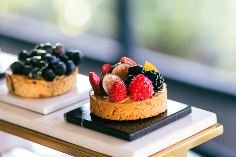 two pastries decorated with fruits and berries on black tray