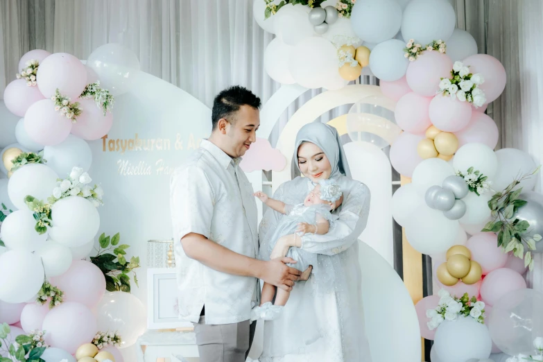 the newly husband holding a baby under a giant balloon arch