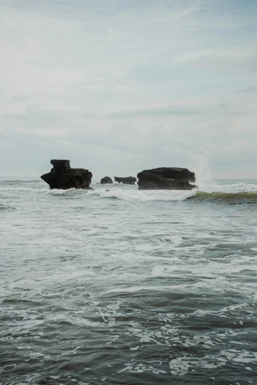 the water is splashing while several rocks are under the ocean