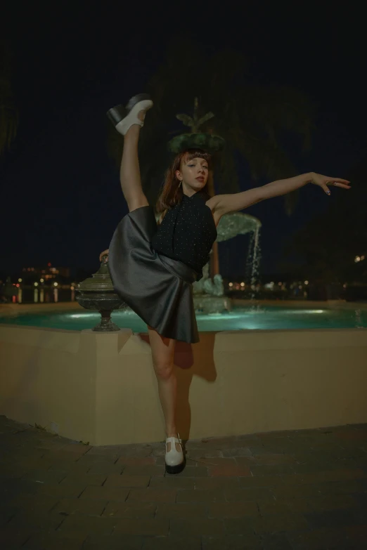 a girl is posing next to a fountain at night