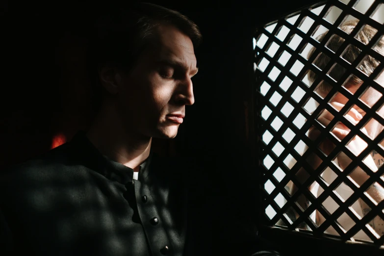 a man looking at the back of his jacket while standing in front of an iron grid window