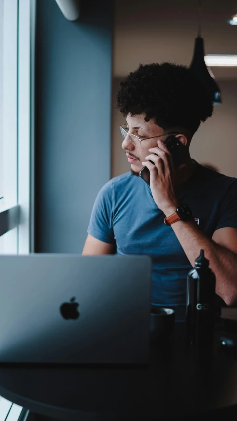 a young man looks at his laptop while talking on a phone