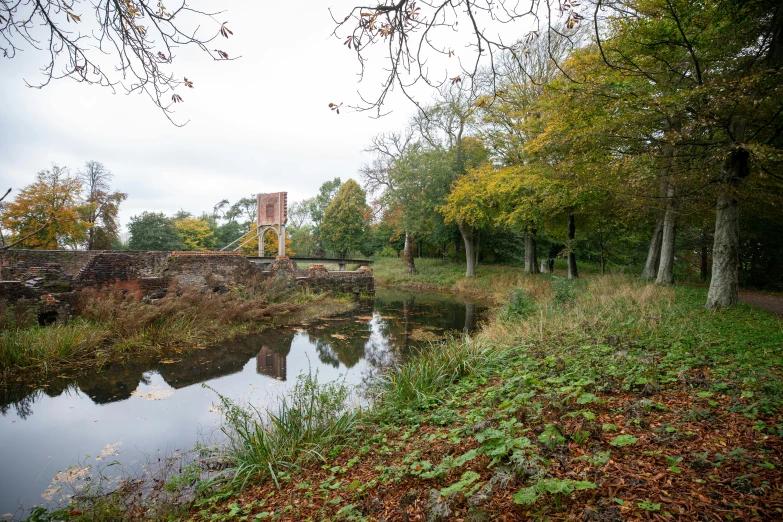 a pond with trees, grass and a bridge across it